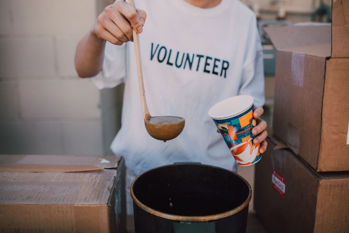 A volunteer serving hot food beside boxes of donated supplies
