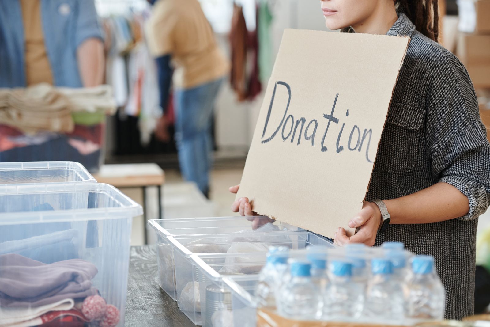 A volunteer holding a donation sign beside crates of supplies and water