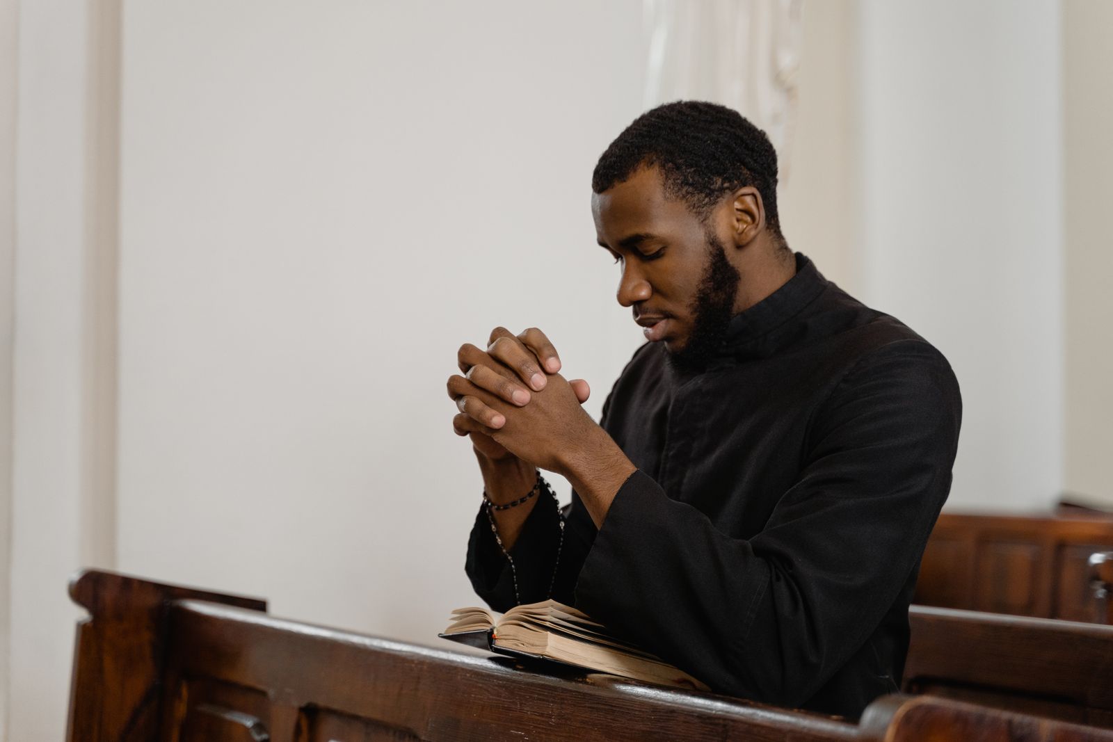 A man praying quietly in a church pew with an open Bible before him