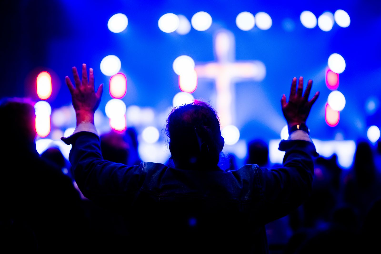 A congregation with hands raised in worship before a lit cross